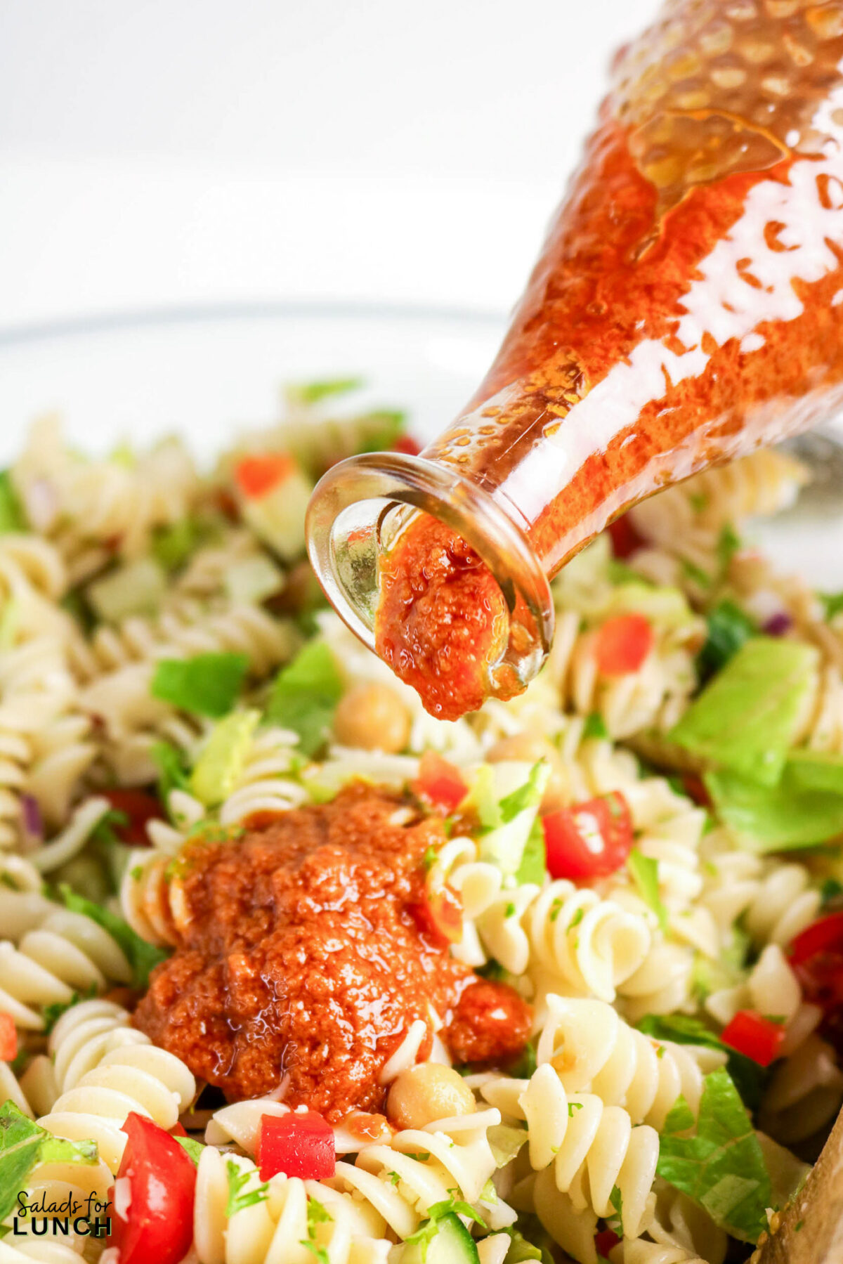 Sundried tomato dressing being drizzled onto a fresh pasta salad with vegetables.