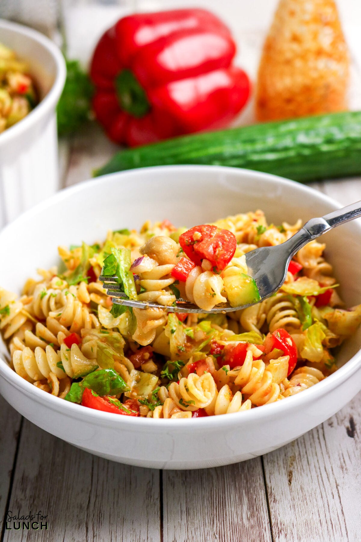 Fork lifting pasta salad with tomatoes, avocado, and chickpeas from a bowl.