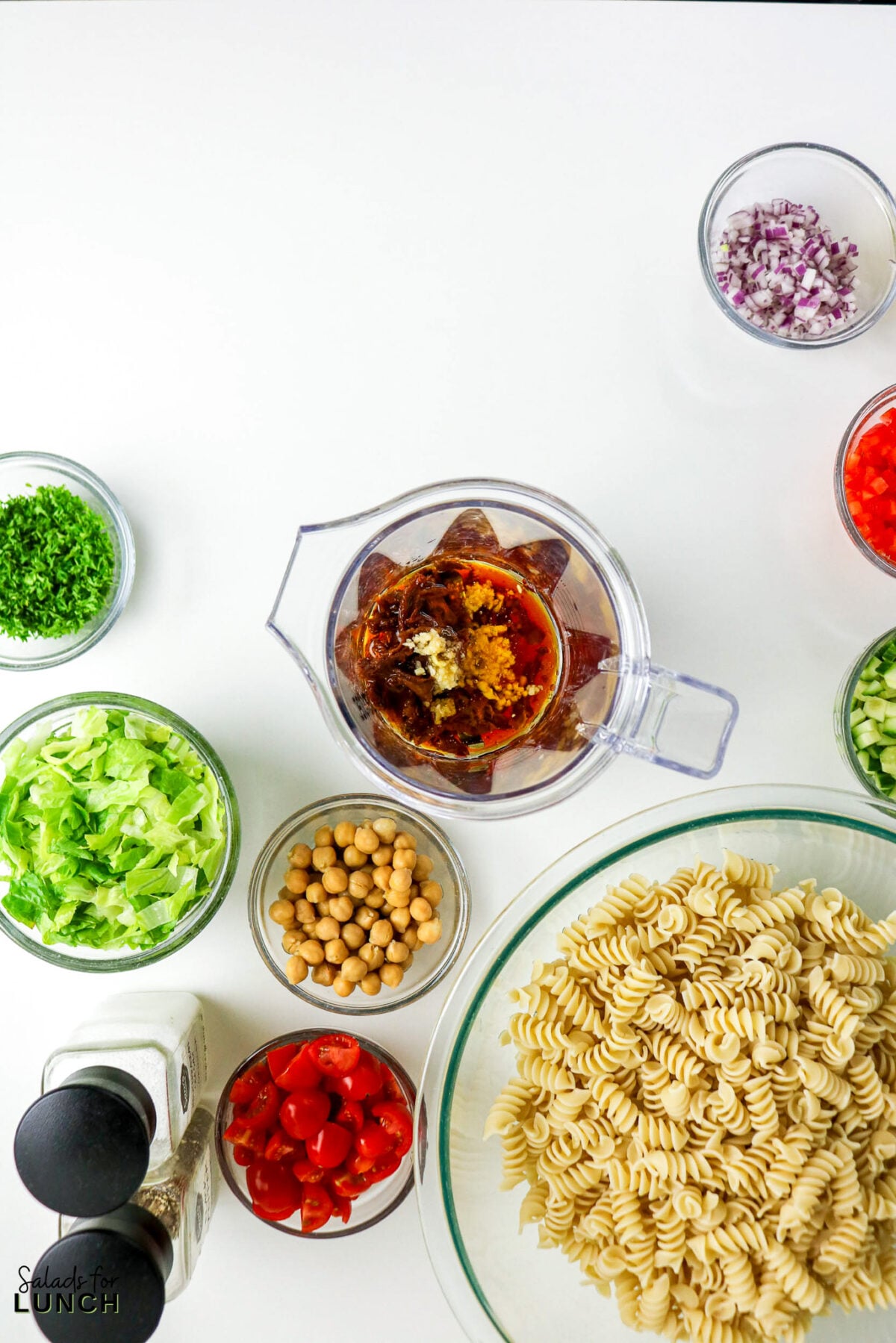 Ingredients for pasta salad: rotini, lettuce, chickpeas, tomatoes, red onion, parsley, and dressing.