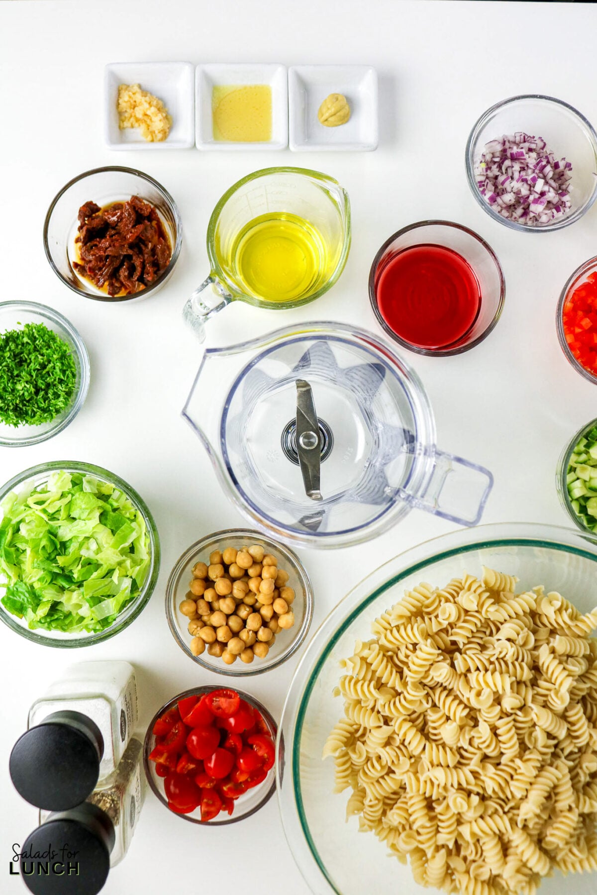 Pasta salad ingredients: fusilli, chickpeas, lettuce, tomatoes, sun-dried tomatoes, red onion, parsley, oil, dressing, garlic, mustard