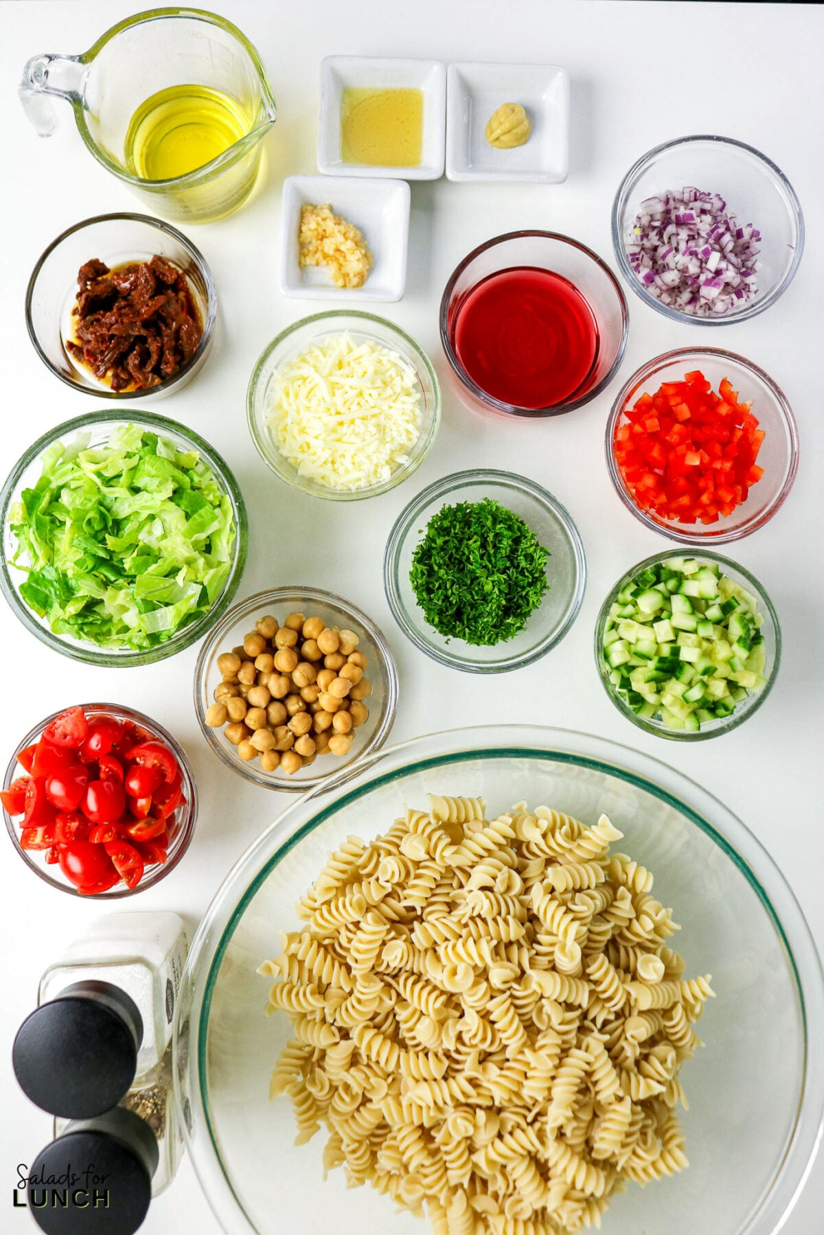 Ingredients for pasta salad including pasta, vegetables, chickpeas, cheese, and dressing