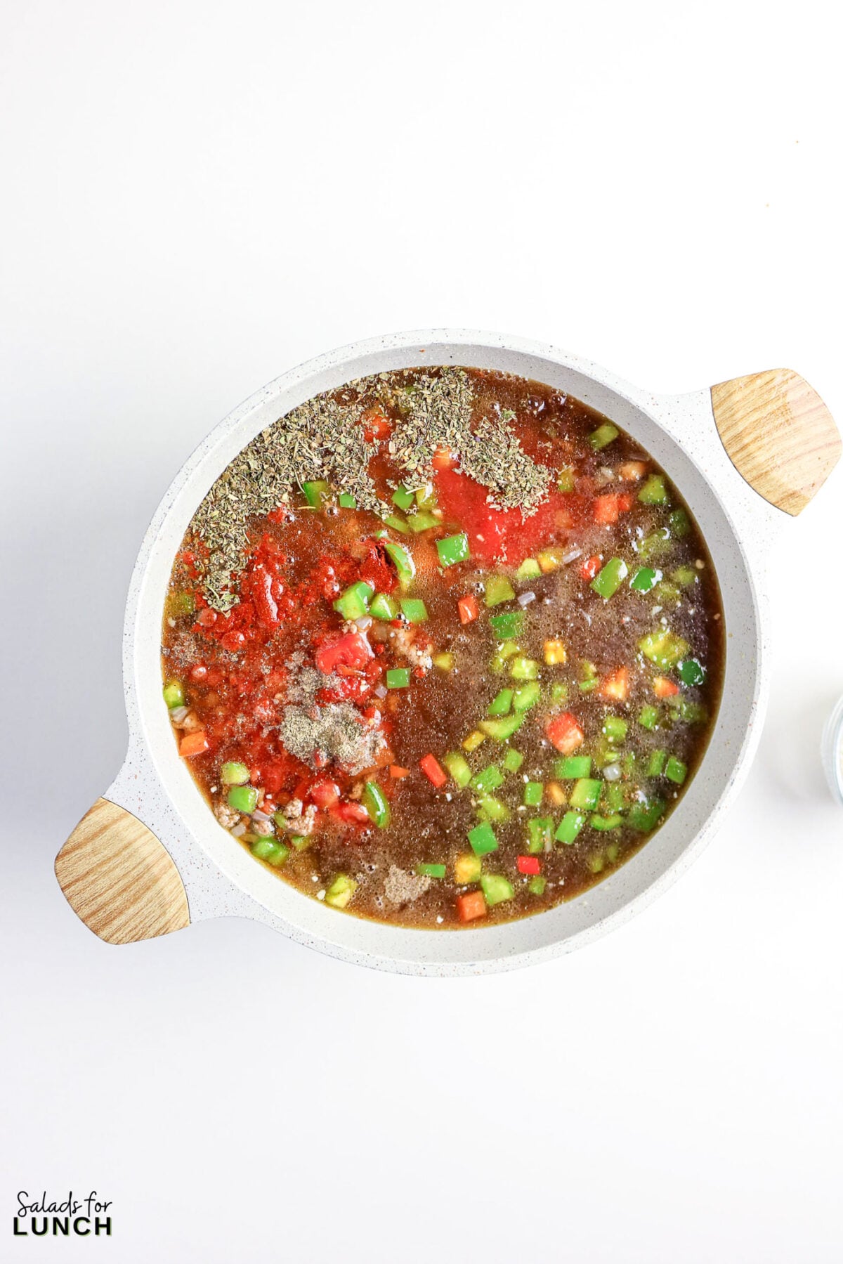 Soup ingredients in a pot, including tomatoes, peppers, and herbs.