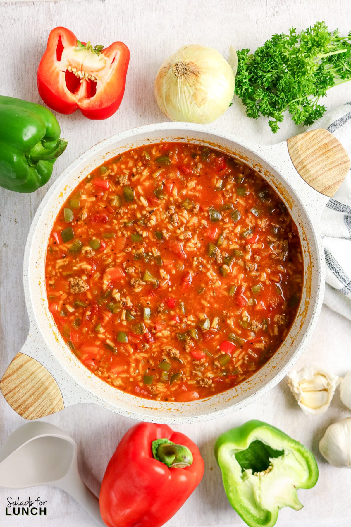 Stuffed pepper soup in pot with peppers, onion, parsley, garlic around.