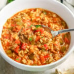 Spoonful of stuffed pepper soup over bowl with rice and ground beef.