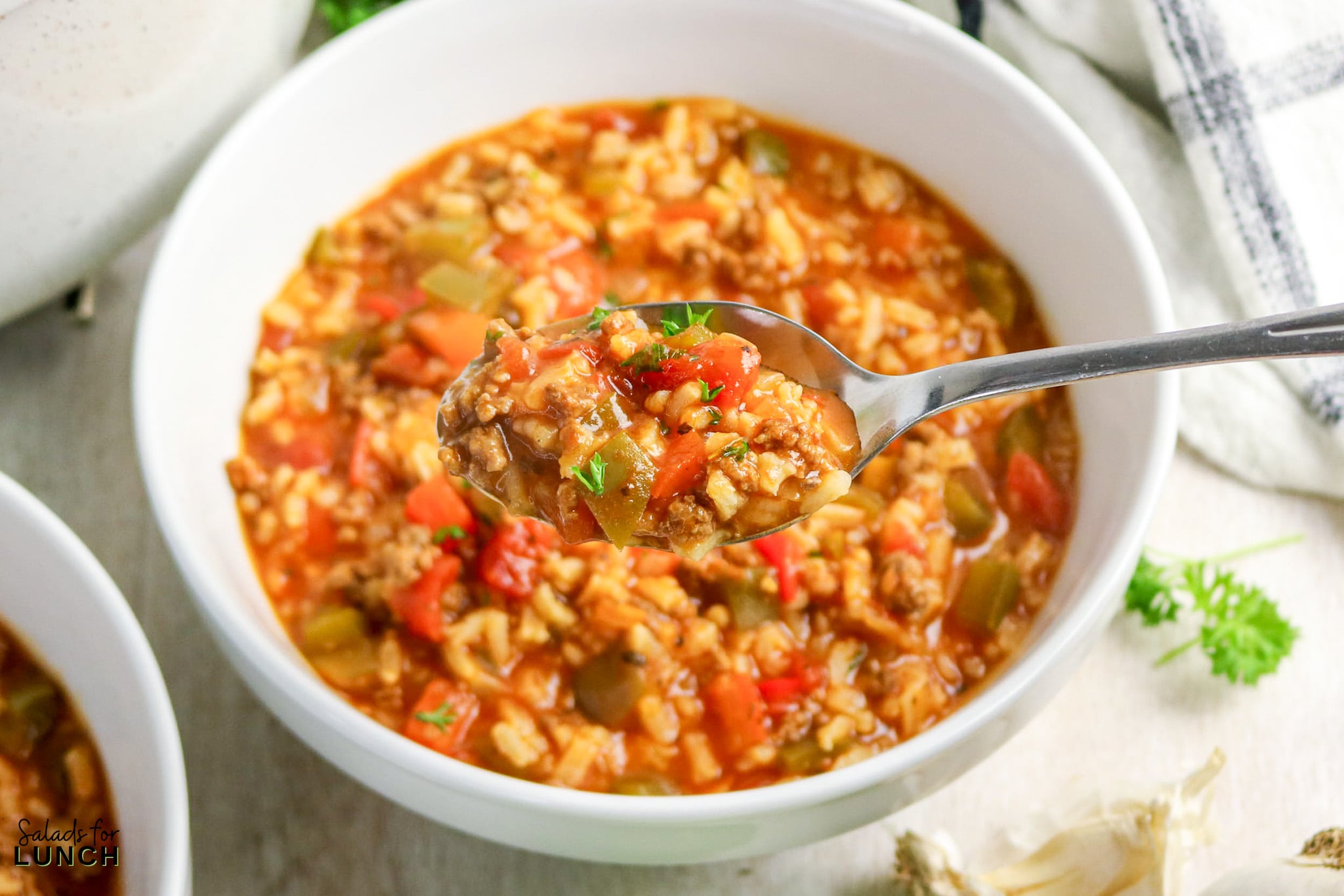 Spoonful of stuffed pepper soup over bowl with rice and ground beef.