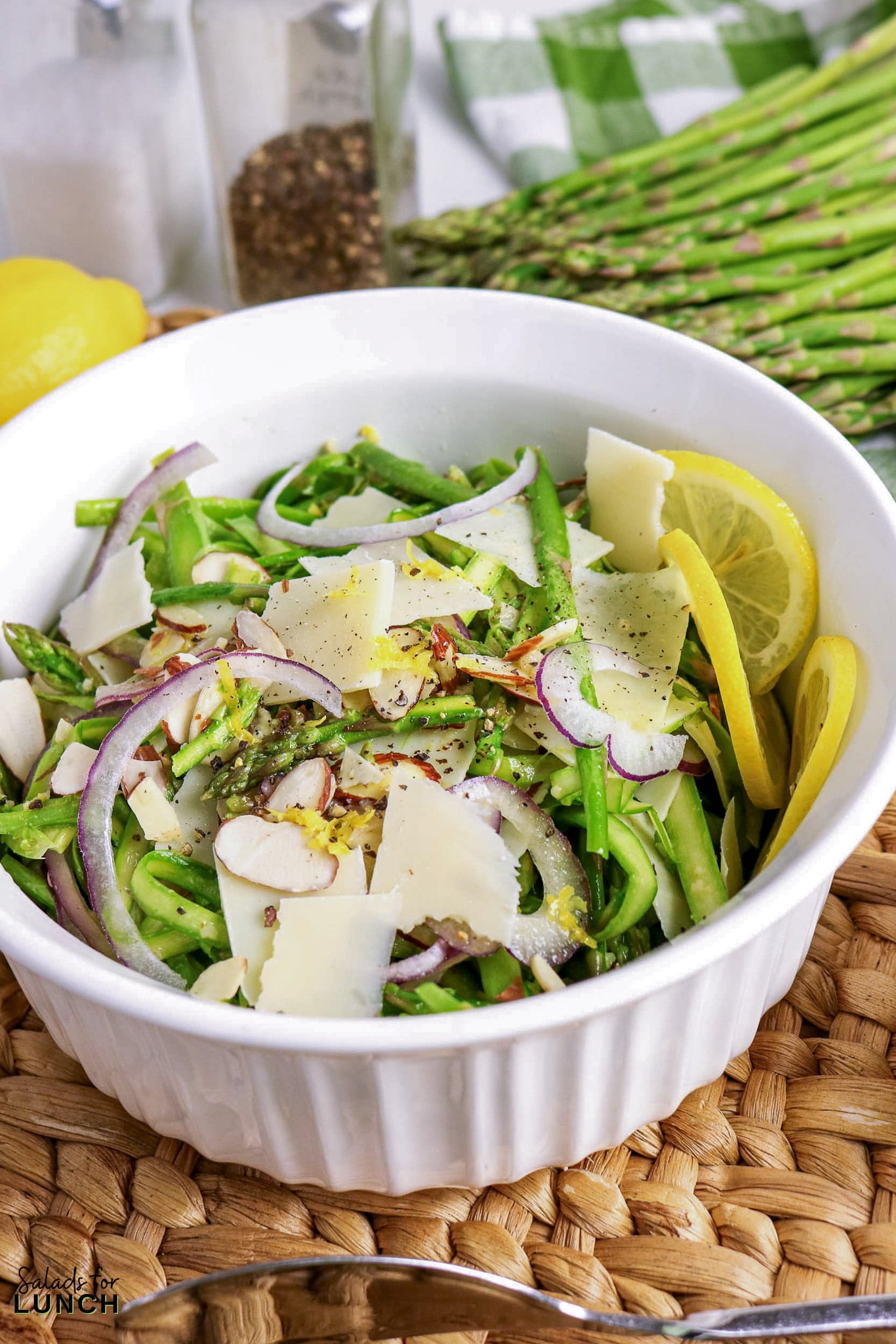 Asparagus salad with shaved parmesan, red onion, and almonds in a white bowl.