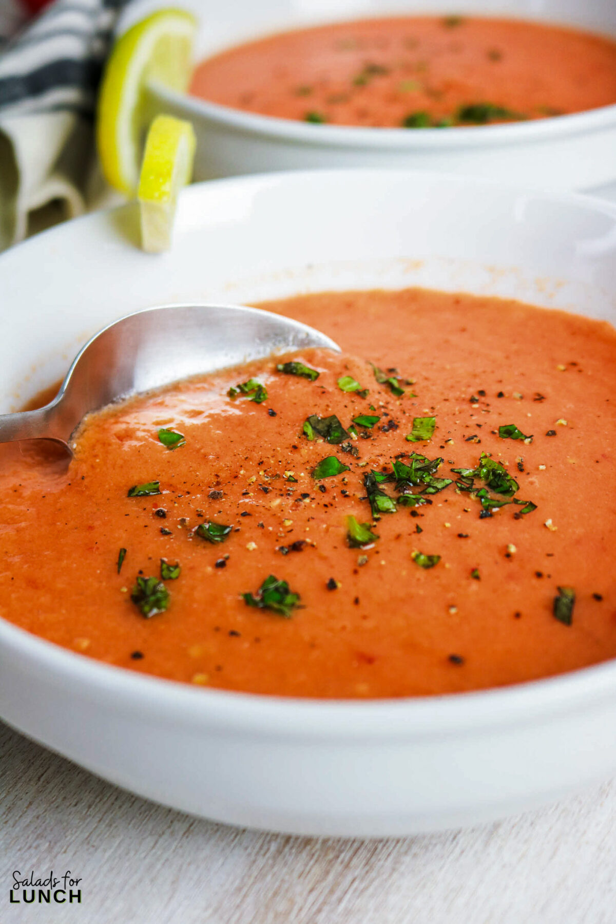 Creamy tomato gazpacho soup in white bowls, garnished with parsley and pepper, with a lime wedge.