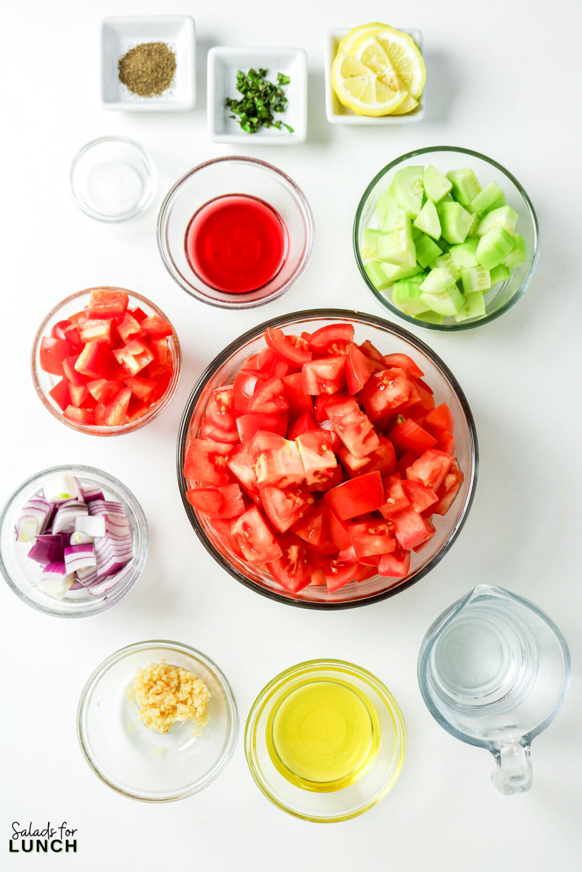 Ingredients for a fresh tomato gazpacho soup: chopped tomatoes, cucumbers, red onion, lemon, and herbs.