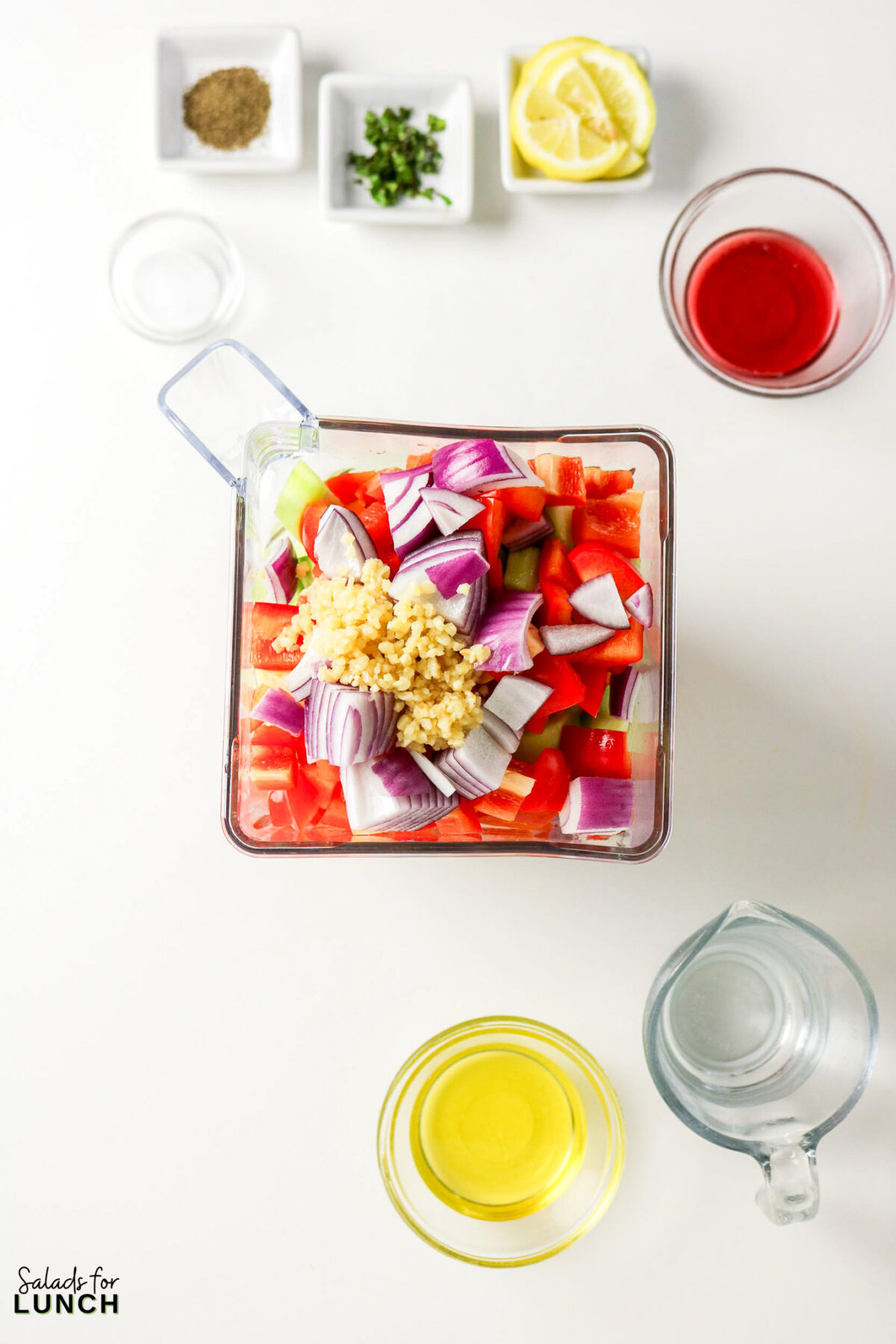 Ingredients for gazpacho in a blender, including tomatoes, cucumber, red onion, and garlic.