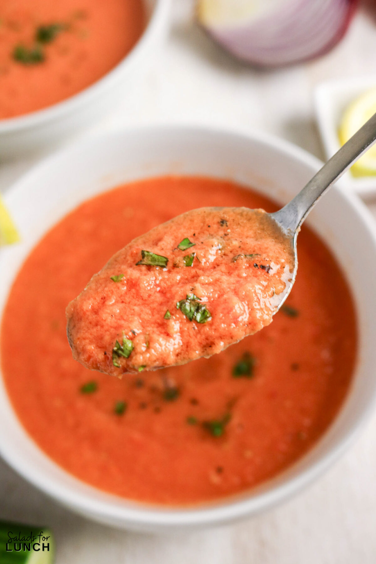 Close-up of gazpacho soup on a spoon, garnished with fresh herbs and black pepper.
