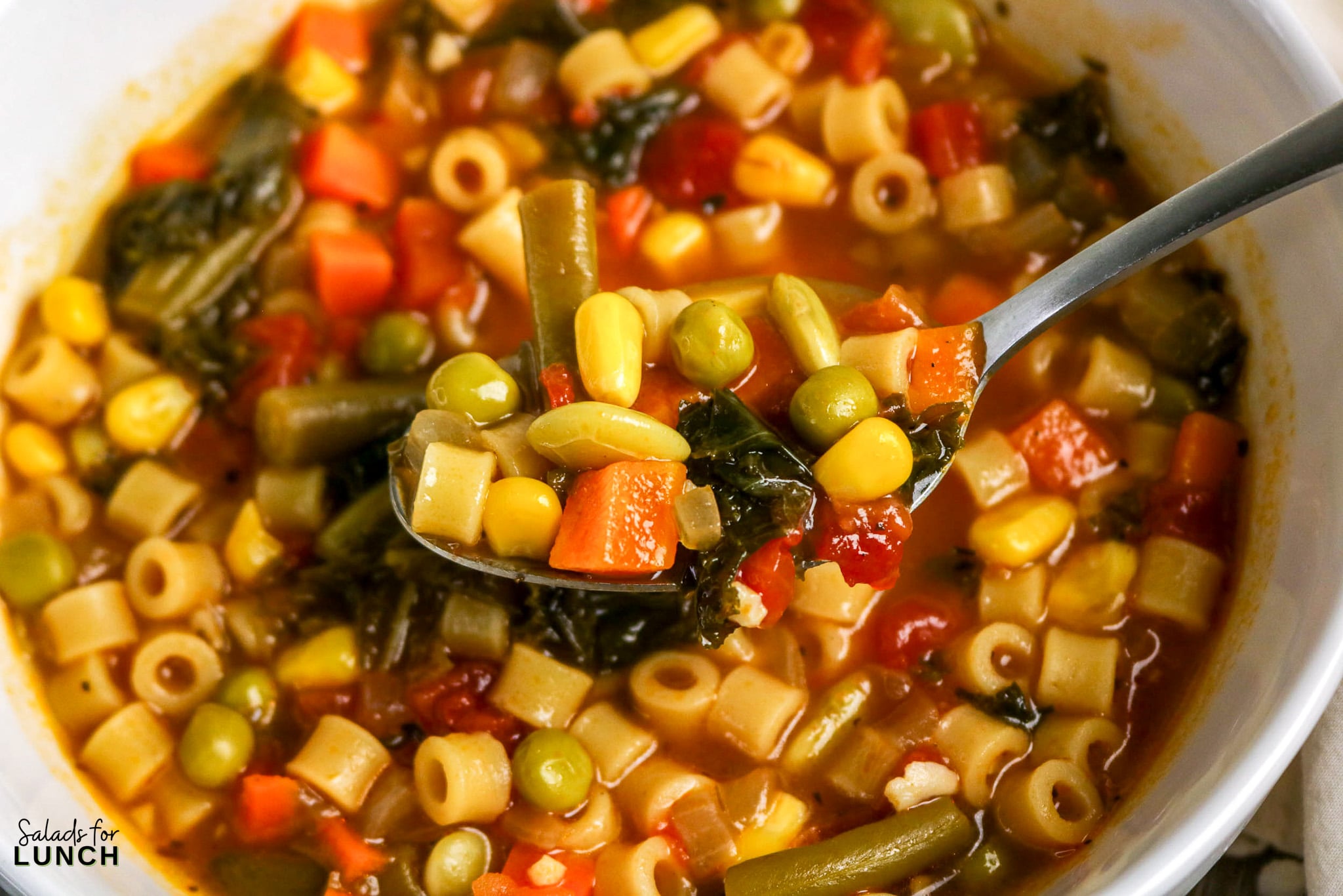 Soupe aux légumes facile dans une seule casserole – Une cuillerée de soupe aux légumes copieuse Gros plan d'une cuillère qui sert une délicieuse soupe de légumes avec des pâtes, du maïs, des pois et des légumes.