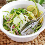 Shaved asparagus salad with parmesan, almonds, and lemon slices in a white bowl.