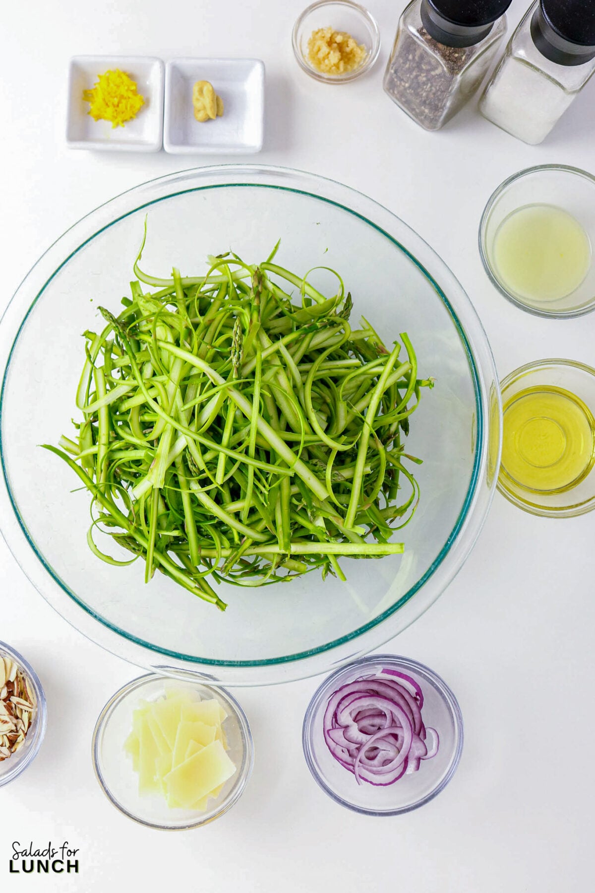 Shaved Asparagus Salad with Lemon Vinaigrette - shaved asparagus salad ingredients overhead Shaved asparagus salad ingredients in bowls: lemon zest, mustard, olive oil, red onion, parmesan, almonds, garlic, herbs, salt, pepper.