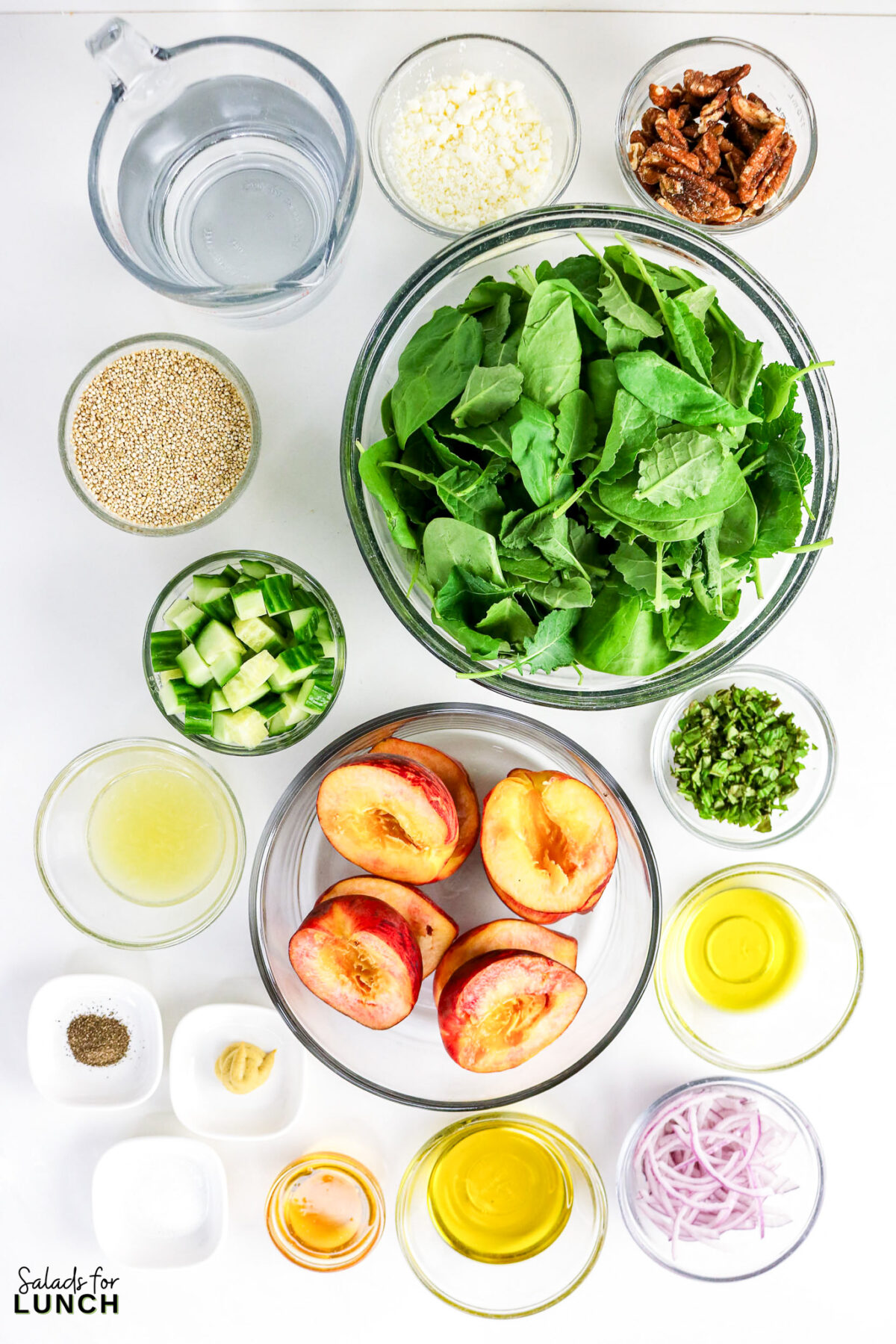 Ingredients for a peach quinoa salad including arugula, halved peaches, quinoa, cucumber, feta, pecans, herbs, and dressing components.