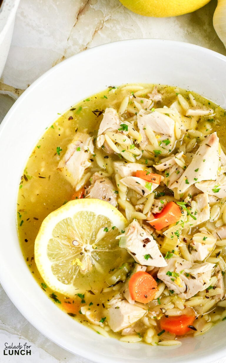 Lemon chicken orzo soup in a white bowl with fresh lemon and herbs