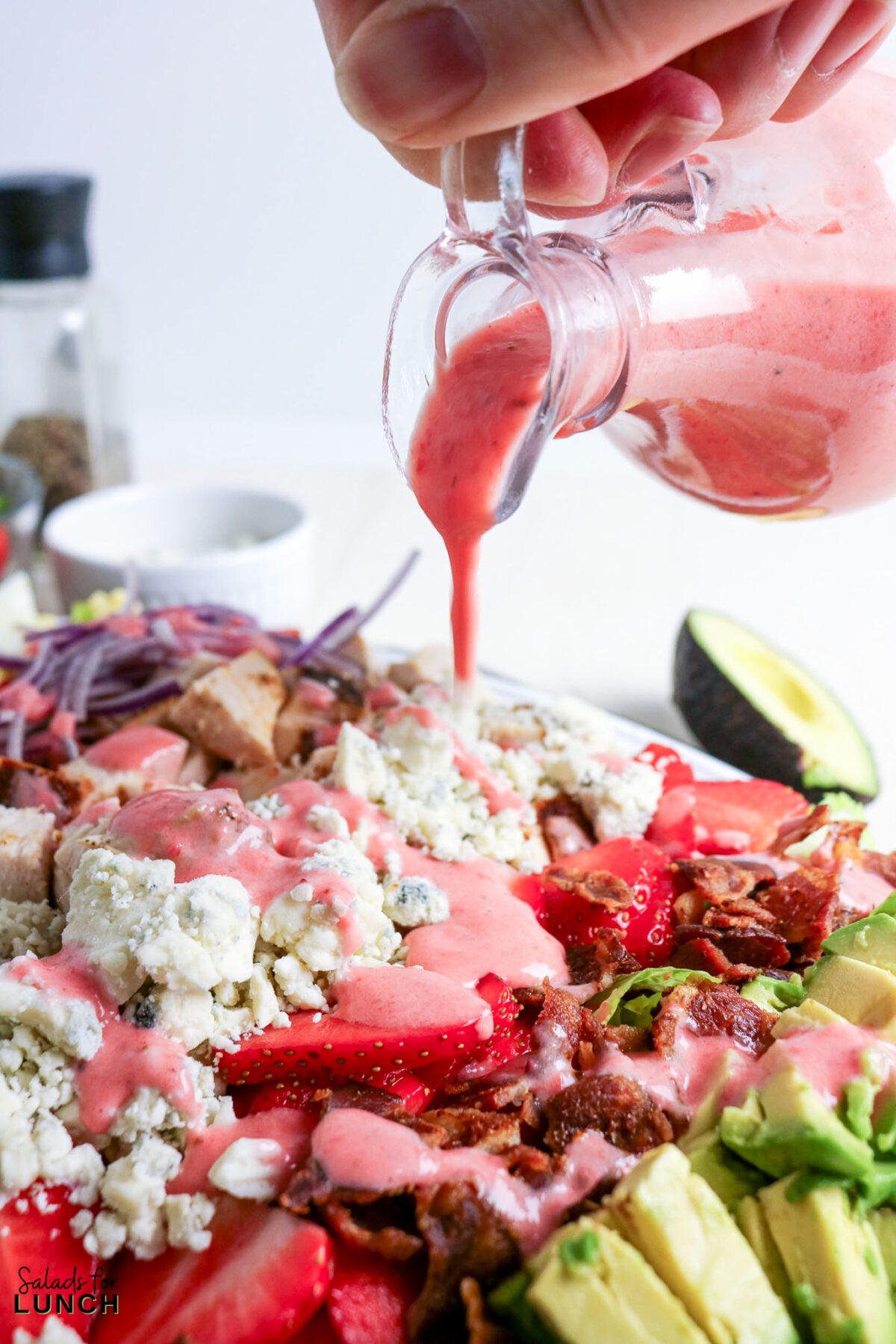 Strawberry Chicken Cobb Salad with Creamy Strawberry Vinaigrette - strawberry chicken salad dressing pour Strawberry chicken salad with blue cheese, bacon, avocado, and dressing being poured.