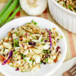 Asian cabbage salad with shredded green and purple cabbage, almonds, sesame seeds, and vegetables served in a white bowl.