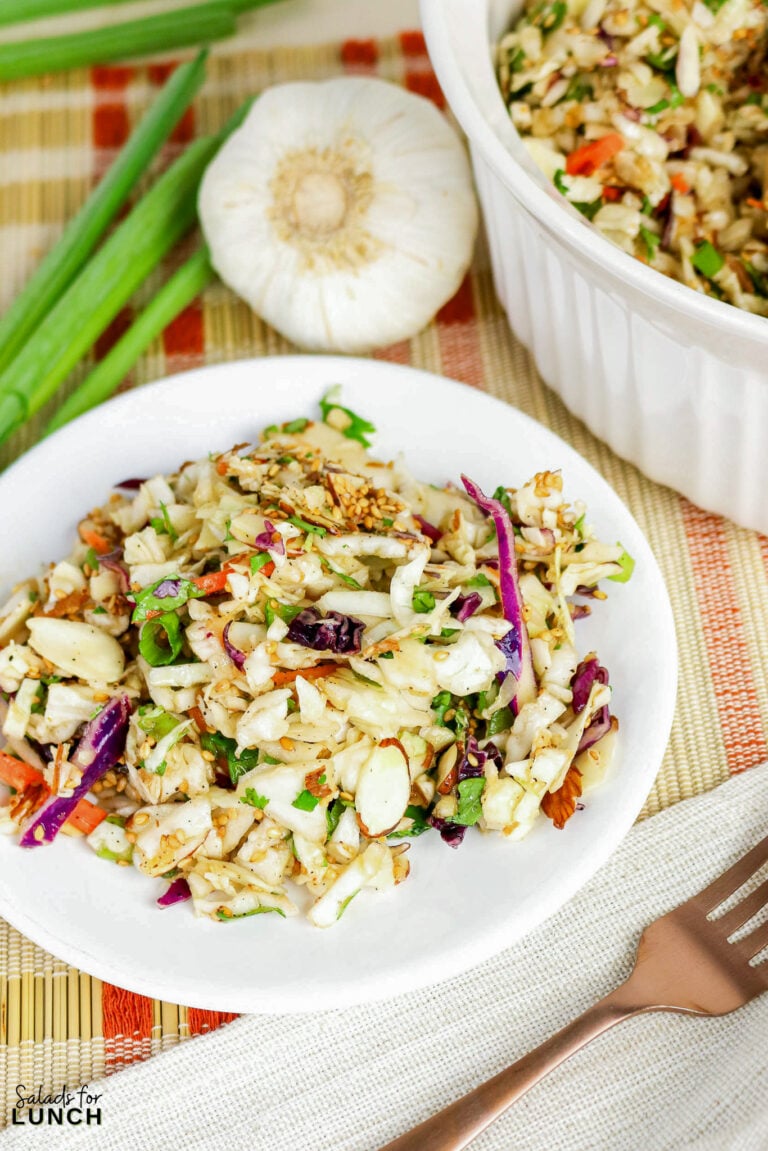Asian cabbage salad with shredded green and purple cabbage, almonds, sesame seeds, and vegetables served in a white bowl.