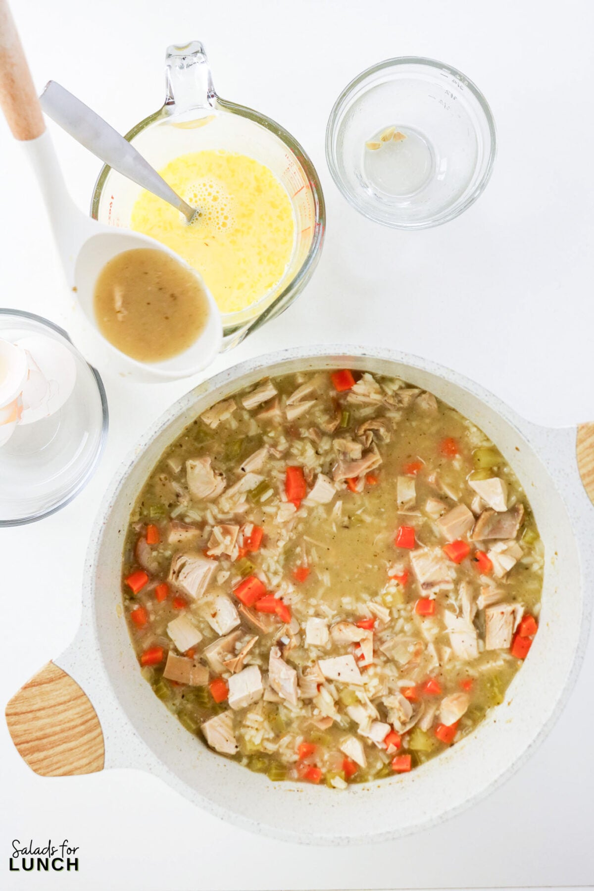 Greek Lemon Chicken and Rice Soup (Easy Avgolemono Recipe) - Greek Lemon Chicken Soup with Rice Recipe 29 Whisked egg and lemon mixture in a measuring cup beside a pot of chicken and rice soup, ready to be tempered and stirred in.