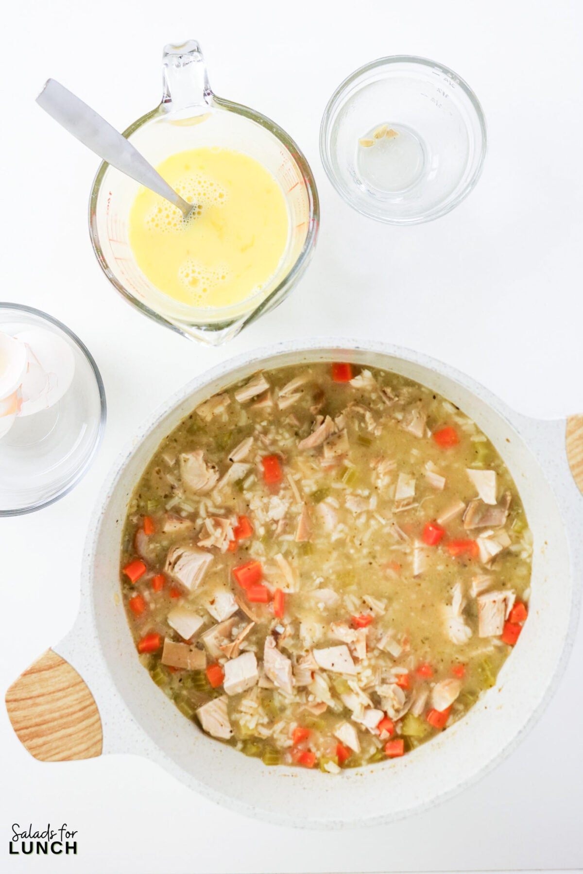 Greek Lemon Chicken and Rice Soup (Easy Avgolemono Recipe) - Greek Lemon Chicken Soup with Rice Recipe 30 Whisked egg and lemon mixture in a measuring cup beside a pot of chicken and rice soup, ready to be tempered and stirred in.