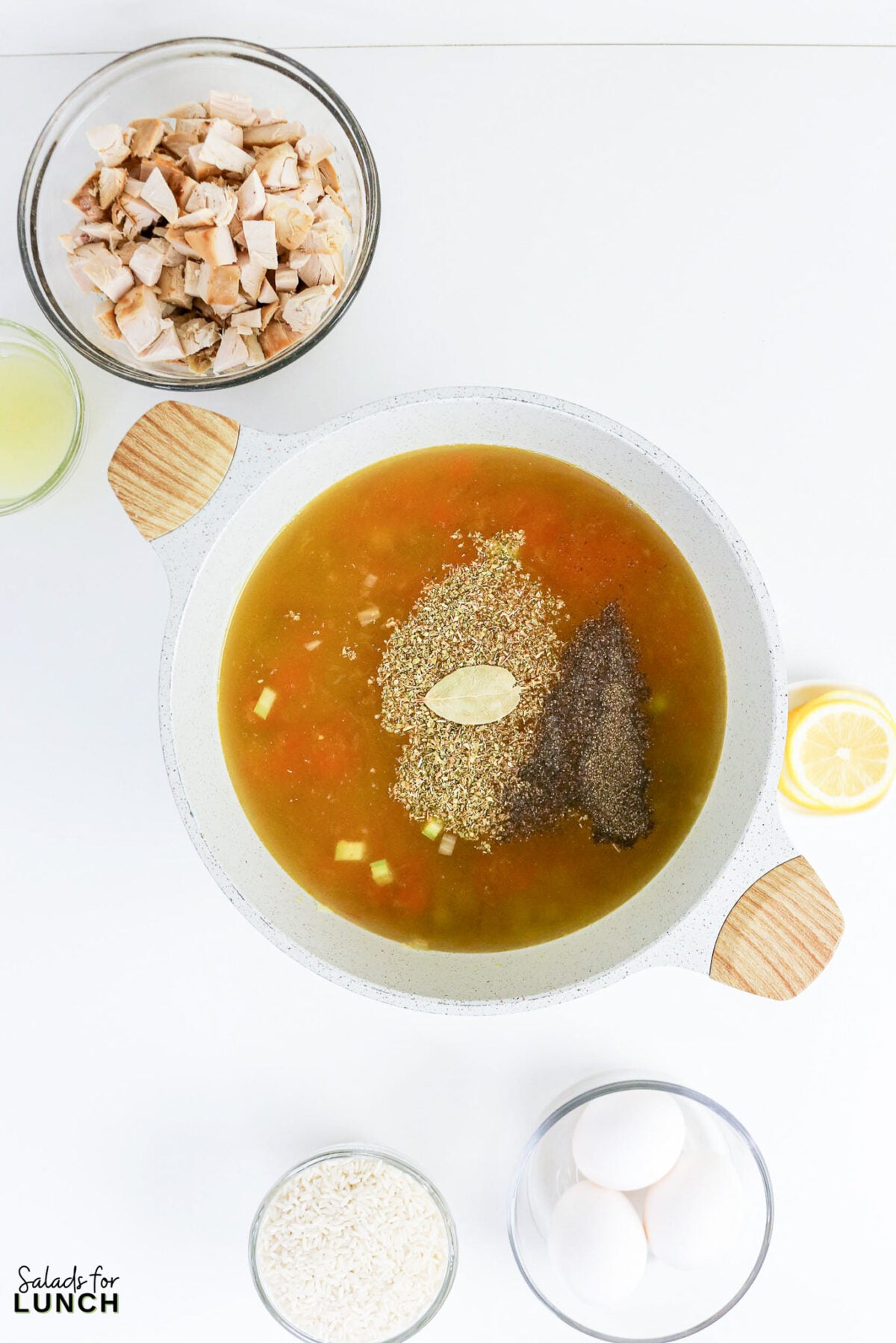 Greek Lemon Chicken and Rice Soup (Easy Avgolemono Recipe) - Greek Lemon Chicken Soup with Rice Recipe 37 Chicken broth with sautéed vegetables, dried oregano, bay leaf, and black pepper in a pot, with shredded chicken, rice, eggs, and lemon nearby.