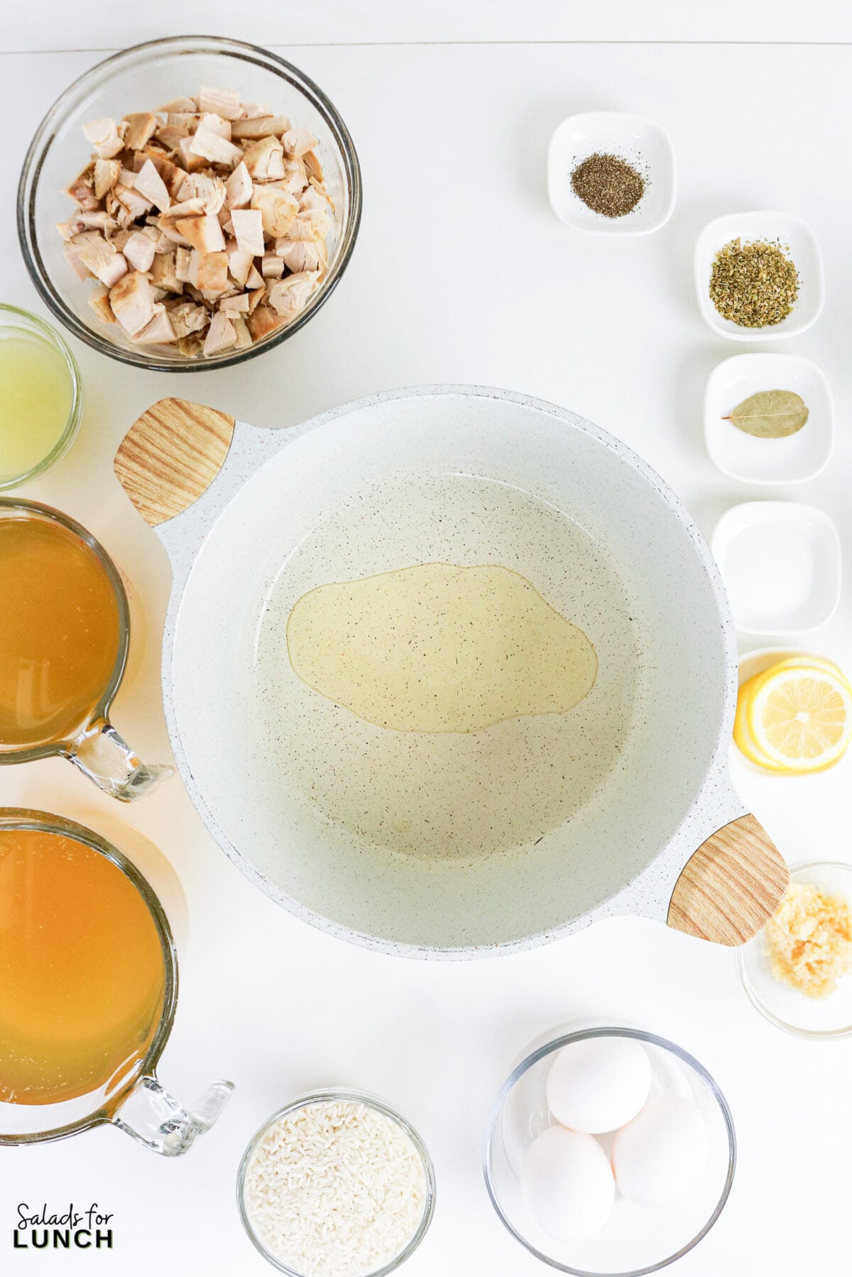 Greek Lemon Chicken and Rice Soup (Easy Avgolemono Recipe) - Greek Lemon Chicken Soup with Rice Recipe 44 Large pot with olive oil surrounded by prepped Greek Lemon Soup ingredients: cooked chicken, broth, rice, eggs, lemon, garlic, oregano, and bay leaf.