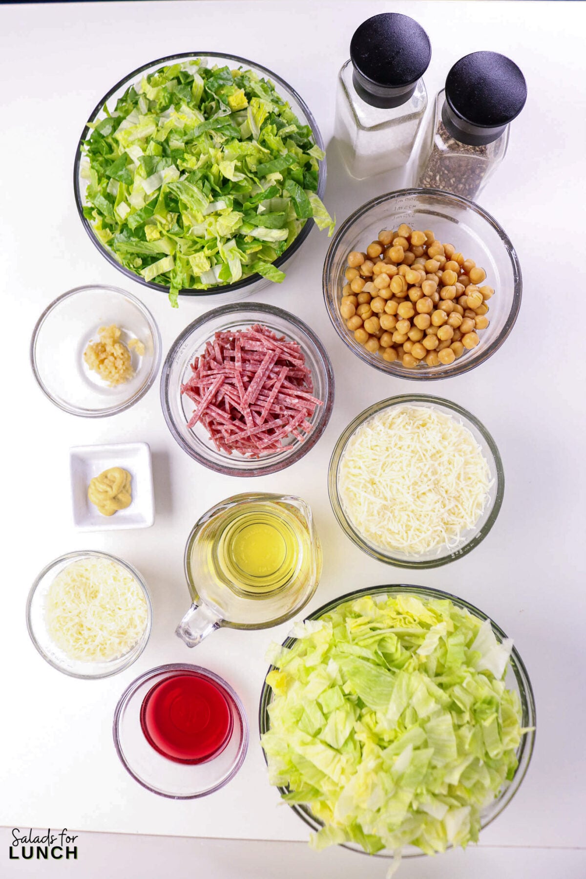 La Scala Chopped Salad Recipe (Easy Beverly Hills Copycat) - Ingredients La Scala Italian Chopped Salad La Scala Salad ingredients laid out in bowls: romaine lettuce, iceberg lettuce, chickpeas, salami strips, shredded cheese, olive oil, red wine vinegar, minced garlic, mustard, salt, and pepper.