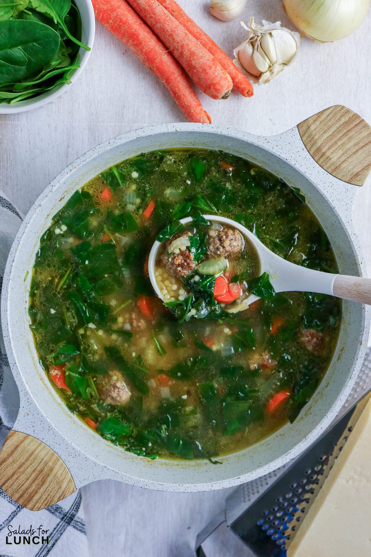 A ladle lifting mini meatballs, spinach, carrots, and tiny pasta from a pot of Italian wedding soup.