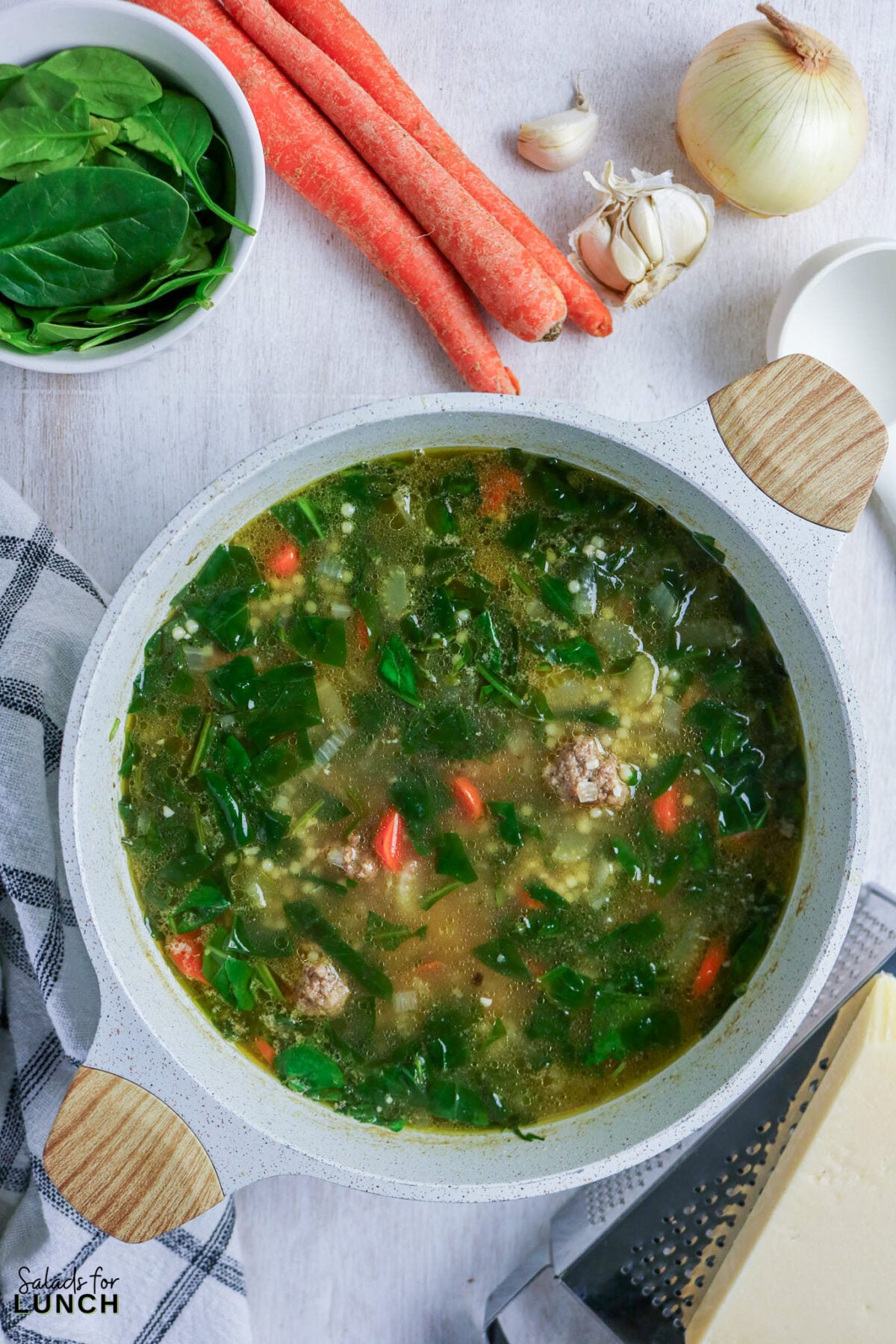 Italian wedding soup simmering in a pot with spinach, mini meatballs, carrots, and tiny pasta in golden chicken broth.