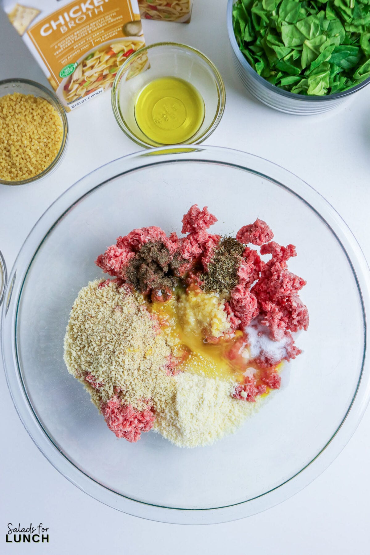 Meatball ingredients combined in a glass bowl: ground meat, breadcrumbs, Parmesan, egg, garlic, and Italian seasoning, with soup ingredients in the background.