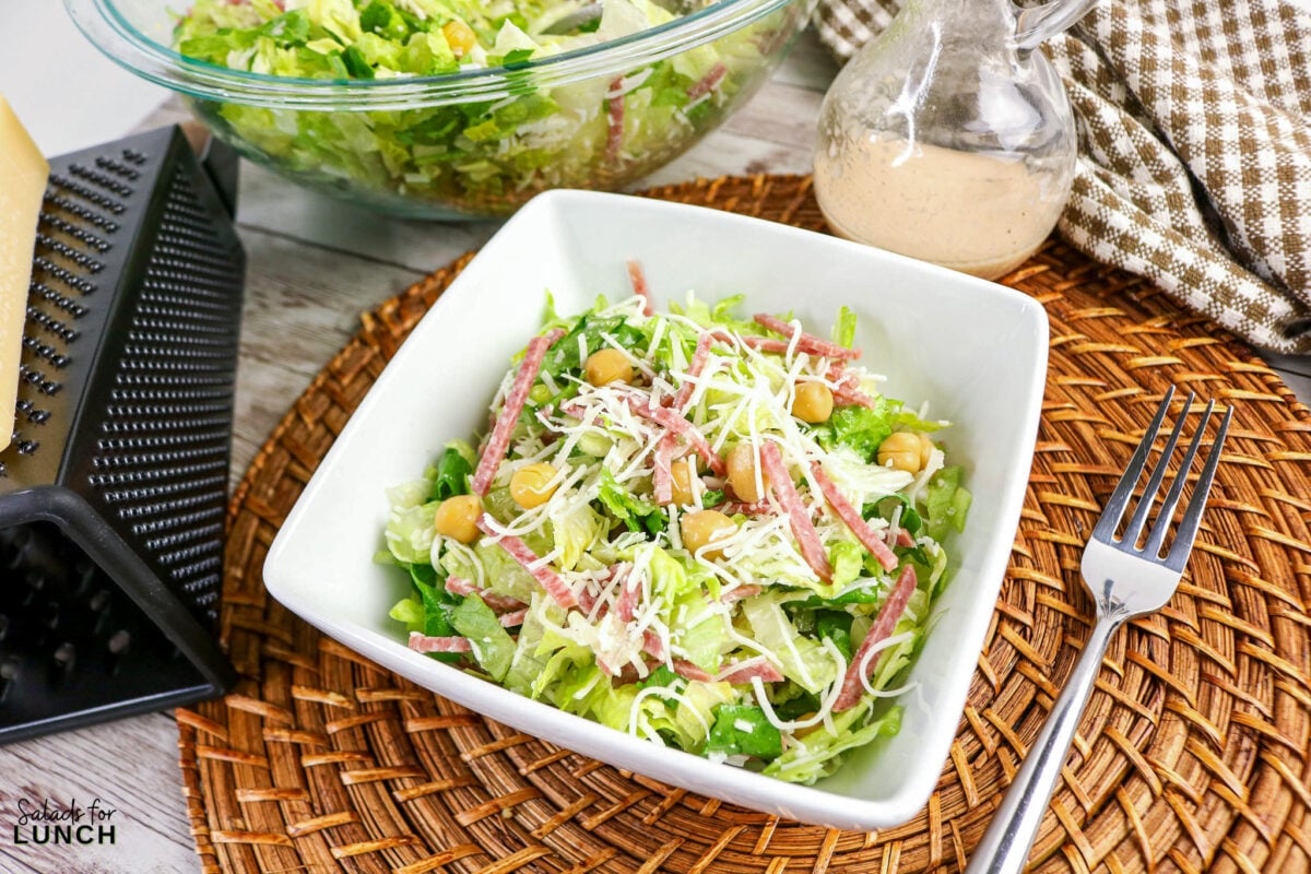 La Scala Chopped Salad Recipe (Easy Beverly Hills Copycat) - La Scala Italian Chopped Salad 11 Chopped Italian salad with romaine, salami strips, chickpeas, and shredded Mozzarella cheese in a white bowl, served with dressing on the side.