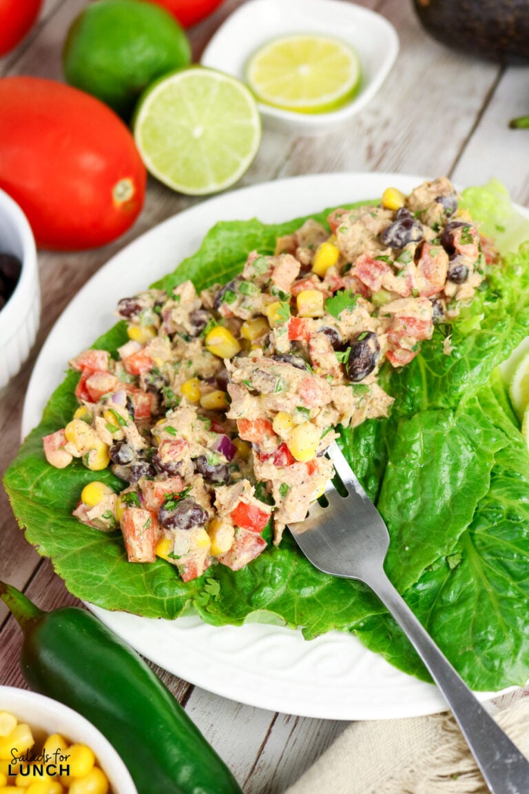 Tuna salad with black beans, corn, and diced tomatoes served on romaine lettuce leaves with a fork.