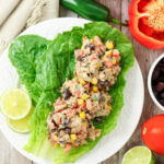 Tuna salad with black beans, corn, and diced red pepper served on romaine lettuce leaves, surrounded by fresh ingredients.