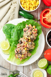 Tuna salad with black beans, corn, and diced red pepper served on romaine lettuce leaves, surrounded by fresh ingredients.