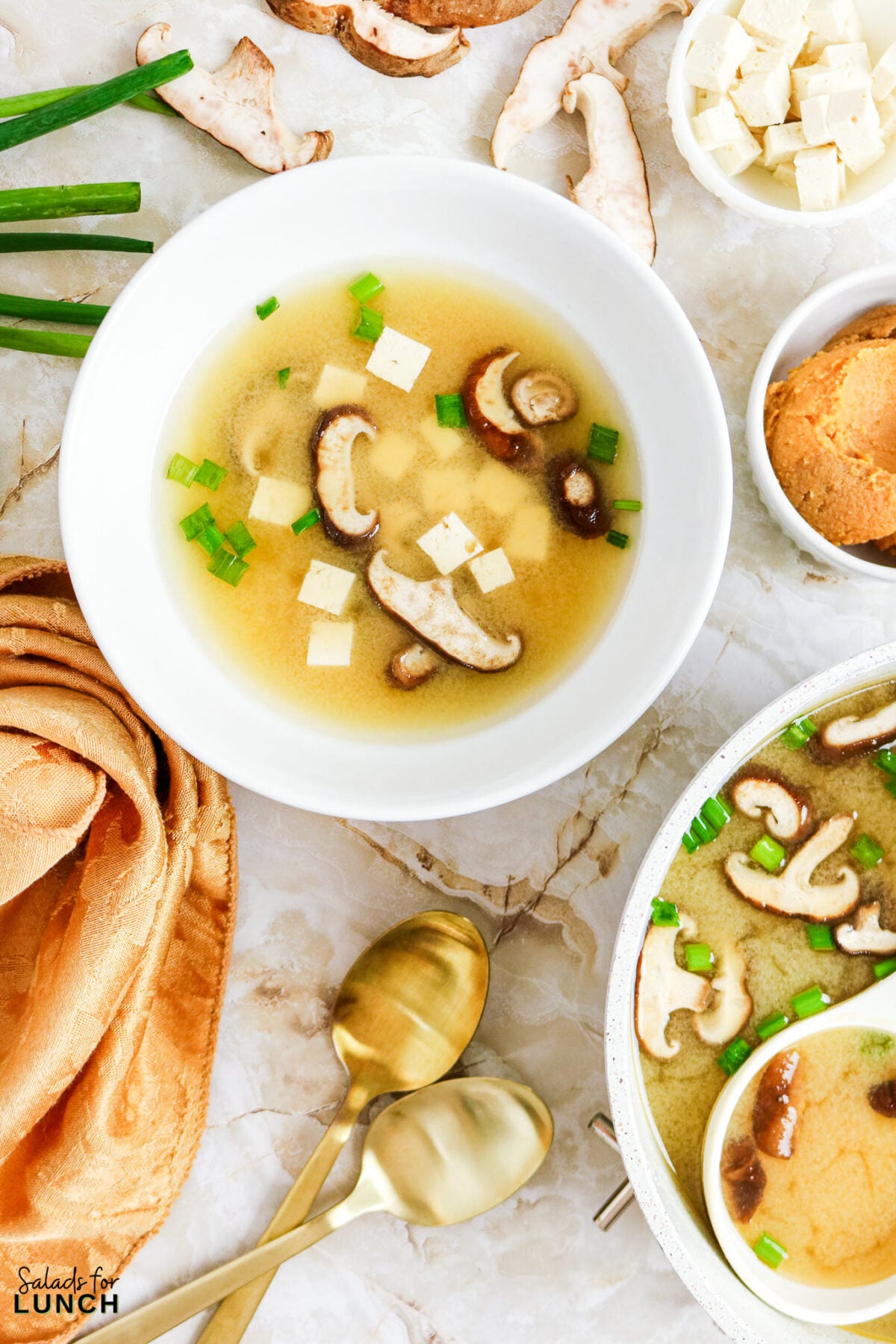 Easy Miso Soup with Mushrooms - Miso Soup Recipe With Mushrooms 14 Miso soup with shiitake mushrooms, tofu cubes, and sliced green onions in a white bowl, surrounded by ingredients.