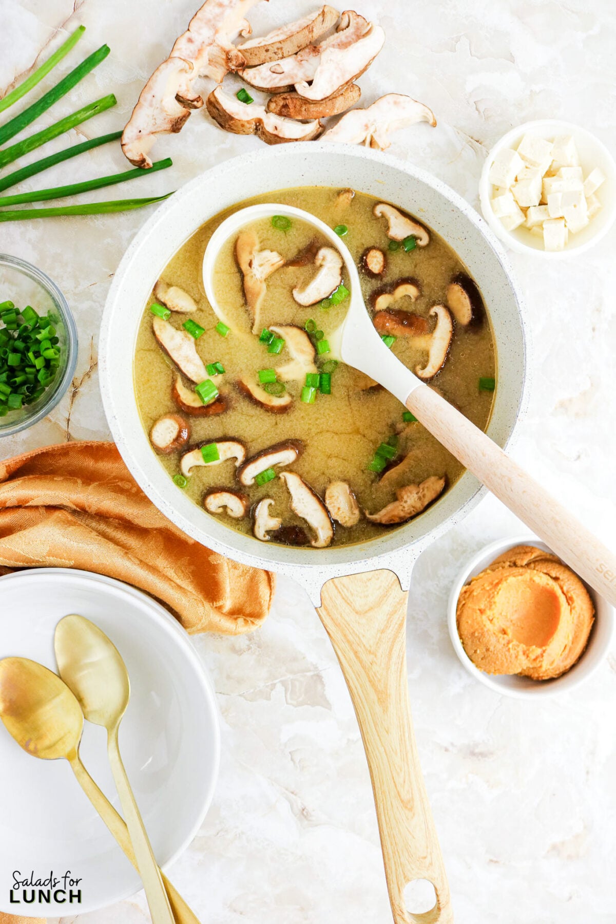 Easy Miso Soup with Mushrooms - Miso Soup Recipe With Mushrooms 19 Miso soup with shiitake mushrooms and green onions in a white pot, surrounded by tofu, miso paste, and fresh ingredients.
