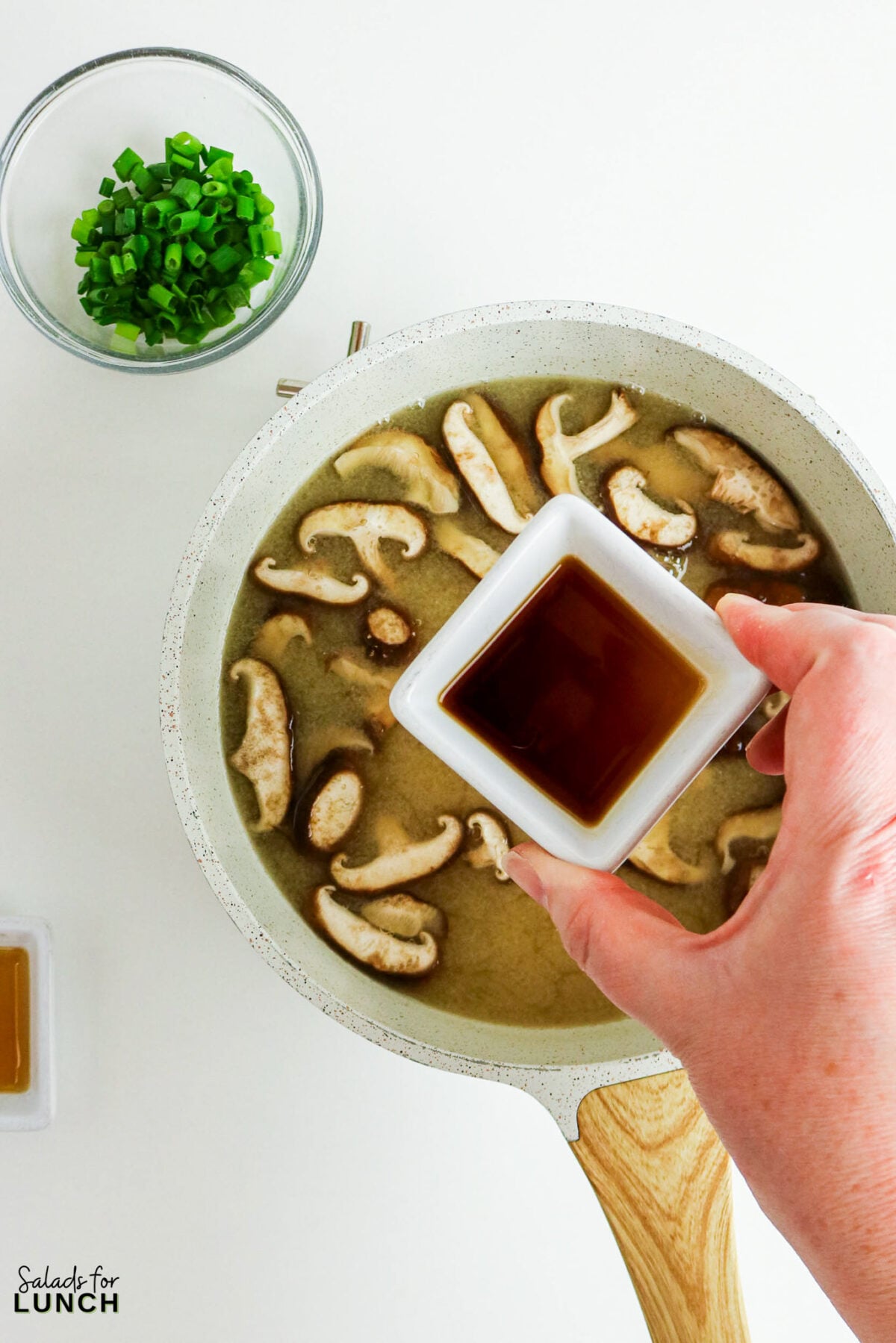Easy Miso Soup with Mushrooms - Miso Soup Recipe With Mushrooms 23 Adding soy sauce to the mushroom miso soup in a saucepan, with sliced green onions in a bowl nearby.