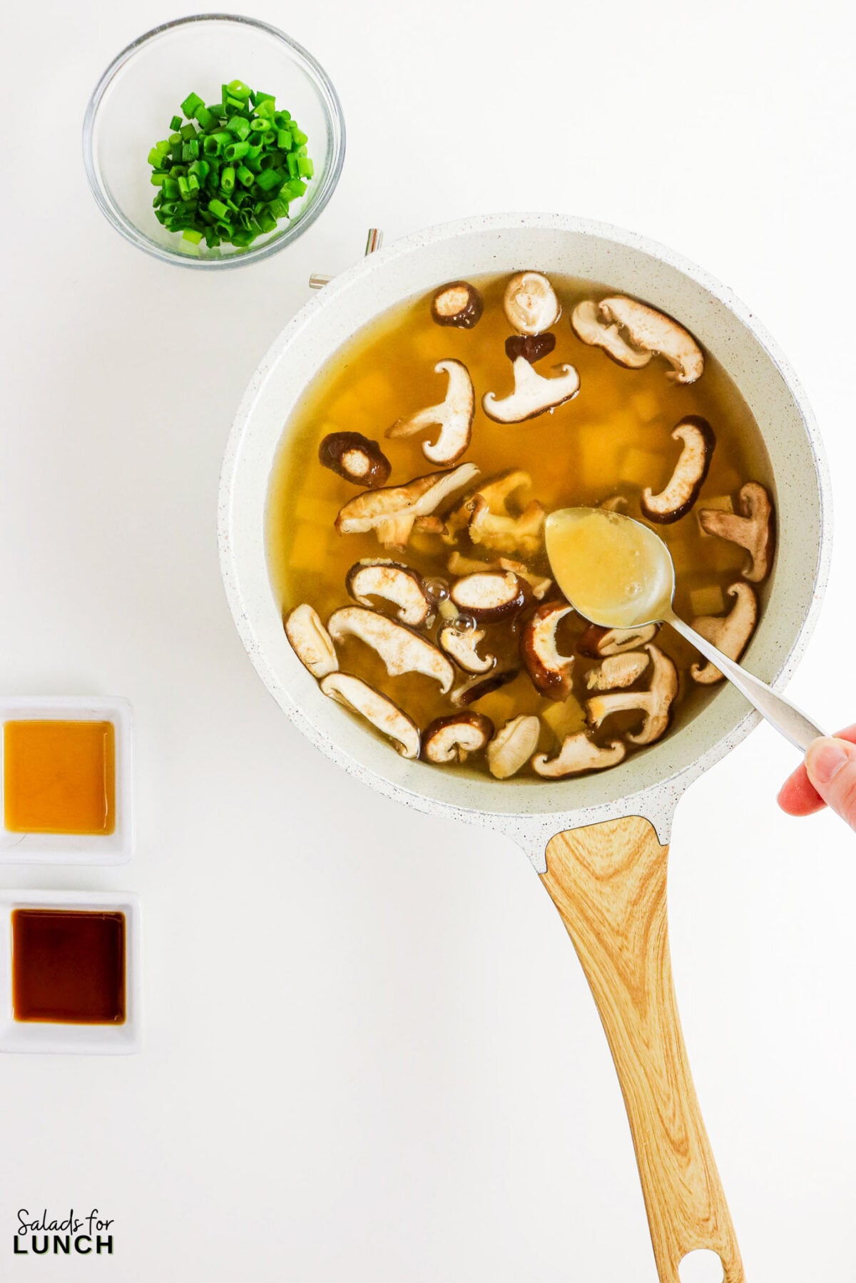 Easy Miso Soup with Mushrooms - Miso Soup Recipe With Mushrooms 25 Ladling hot broth from the pot of mushroom miso soup, with sliced green onions, sesame oil, and soy sauce alongside.
