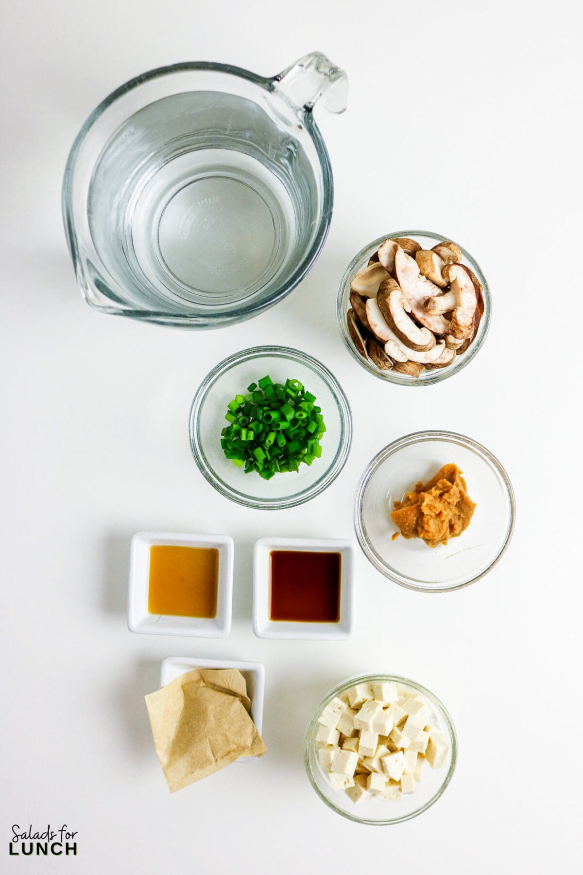 Easy Miso Soup with Mushrooms - Miso Soup Recipe With Mushrooms 34 Miso soup ingredients laid out overhead: water, sliced mushrooms, green onions, miso paste, soy sauce, dashi, tofu cubes, and dashi packet.