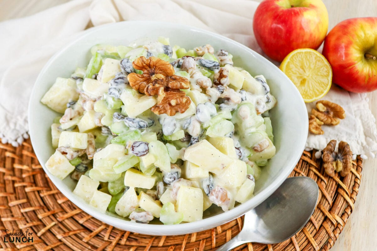 Apple, Celery & Walnut Crunch Salad - Process Apple Celery Walnut Salad 1 Apple, celery and walnut crunch salad in a white bowl, topped with a whole walnut, with fresh apples and lemon half alongside.