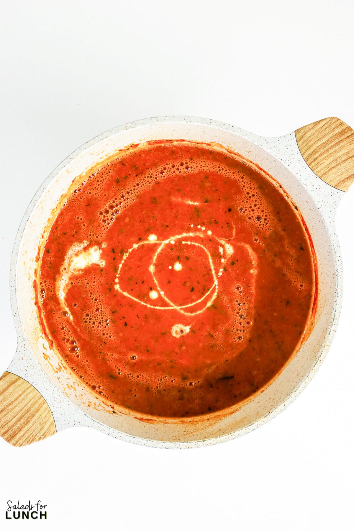 Blended roasted tomato basil soup with a swirl of cream in a large pot, ready to serve.
