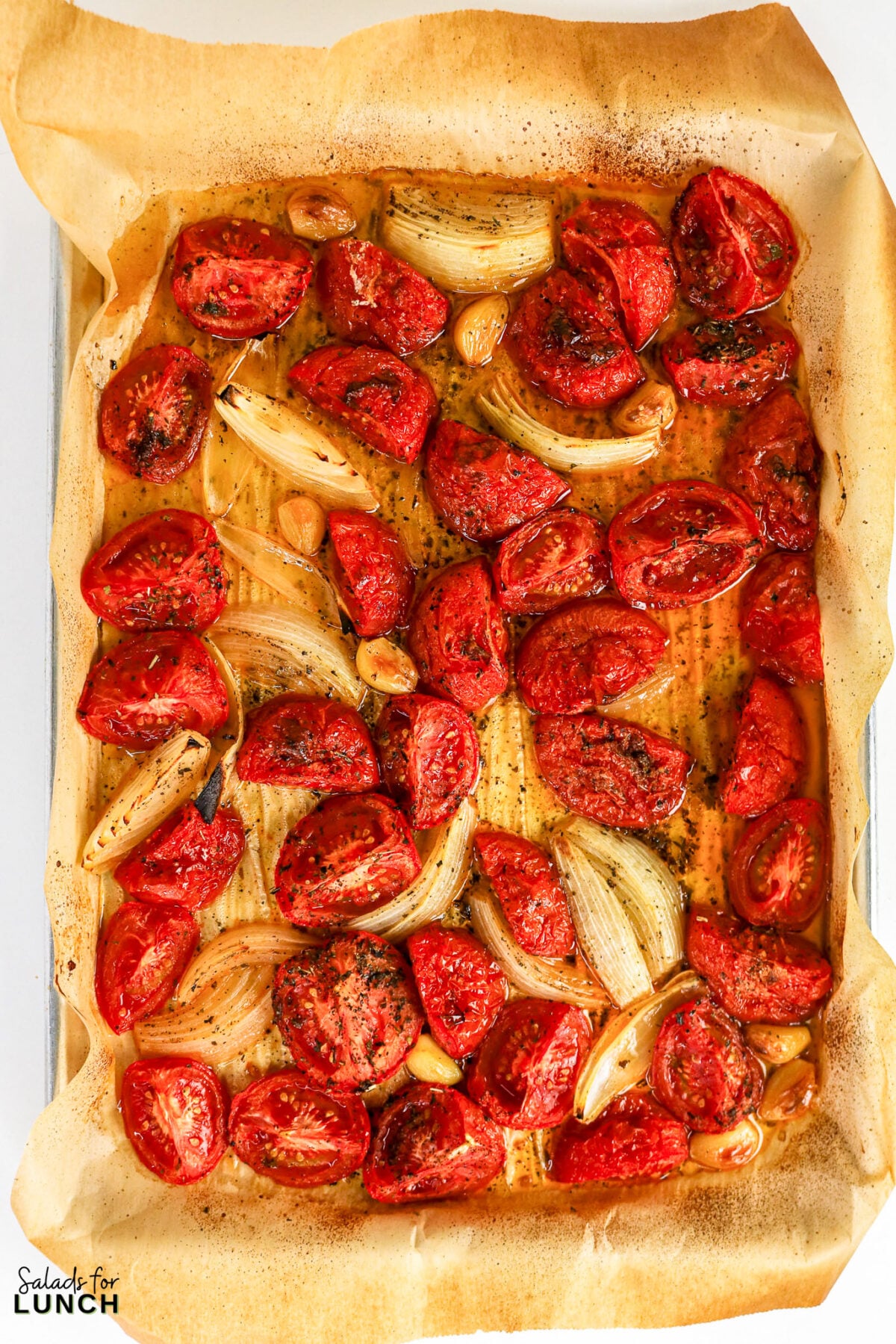 Caramelized tomato quarters, onion wedges, and garlic cloves roasted on a parchment-lined sheet pan until collapsed and golden.