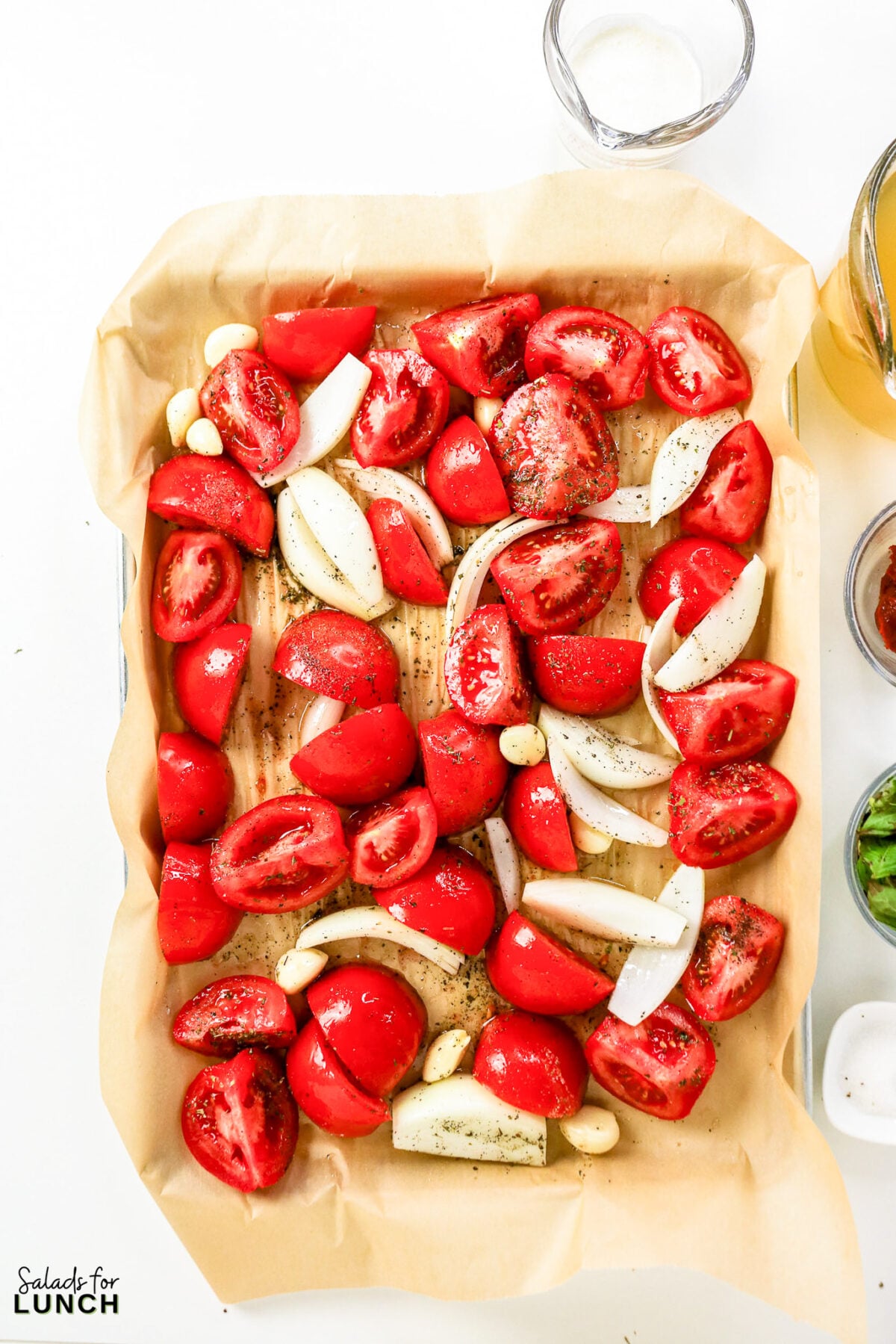 Tomato quarters, onion wedges, and garlic cloves seasoned with Italian seasoning on a parchment-lined baking sheet, ready to roast.