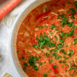Pot of Thai Coconut Curry Soup with shredded chicken, tomatoes, and cilantro, garnished with parsley.