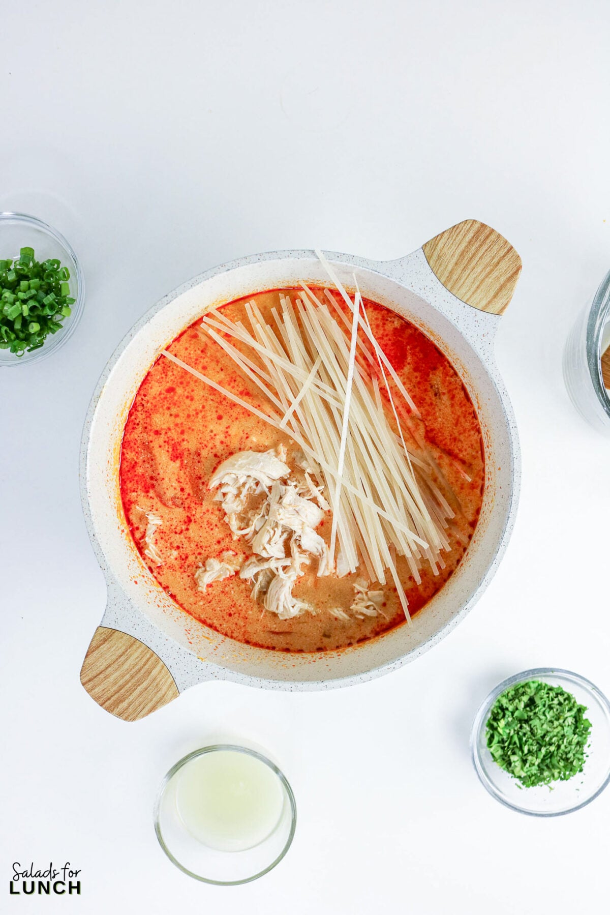 Shredded chicken and dry rice noodles added to the coconut curry broth in the pot before simmering.