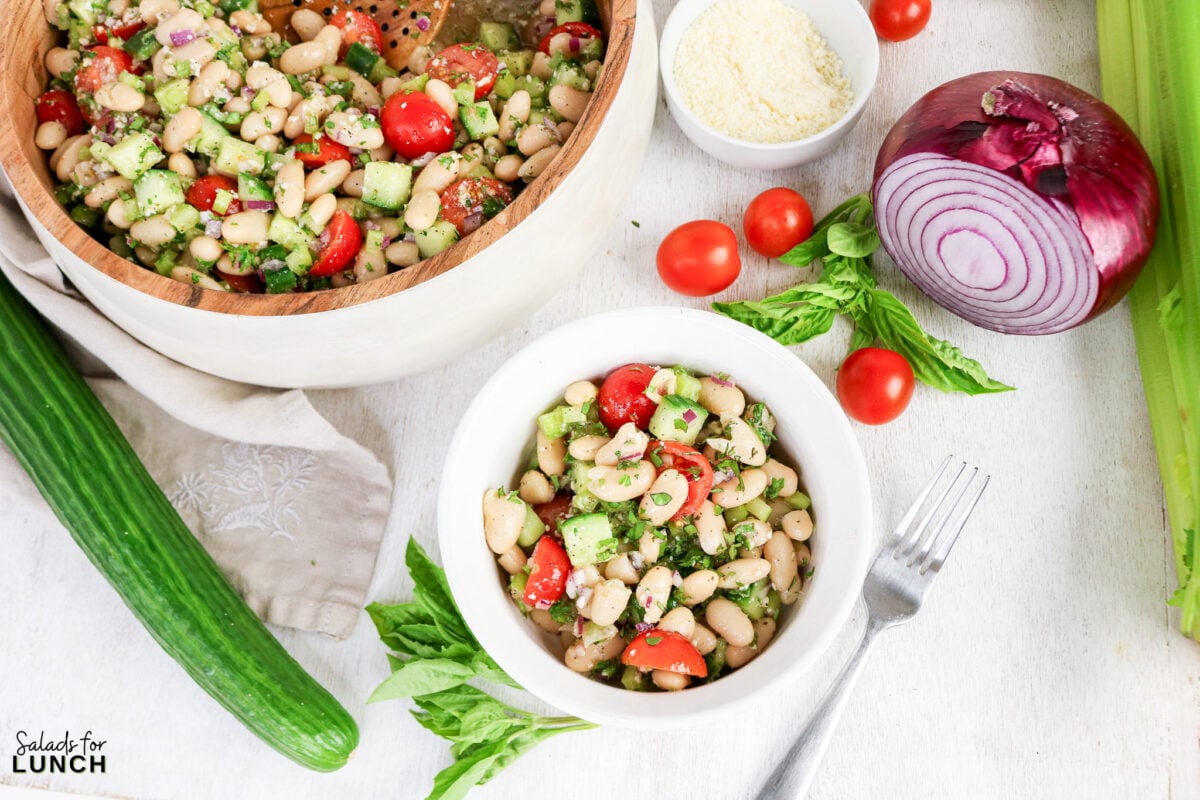 Easy Tuscan Bean Salad - Tuscan Bean Salad Hero 08 Tuscan bean salad with cherry tomatoes, cucumber, red onion, and fresh basil served in a bowl and a large wooden mixing bowl.