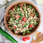 White bean salad with cherry tomatoes, cucumber, and herbs in a wooden bowl, surrounded by fresh ingredients.