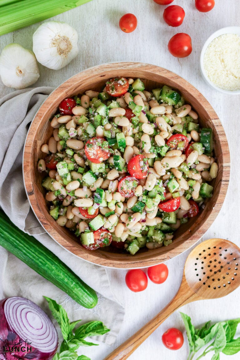 White bean salad with cherry tomatoes, cucumber, and herbs in a wooden bowl, surrounded by fresh ingredients.