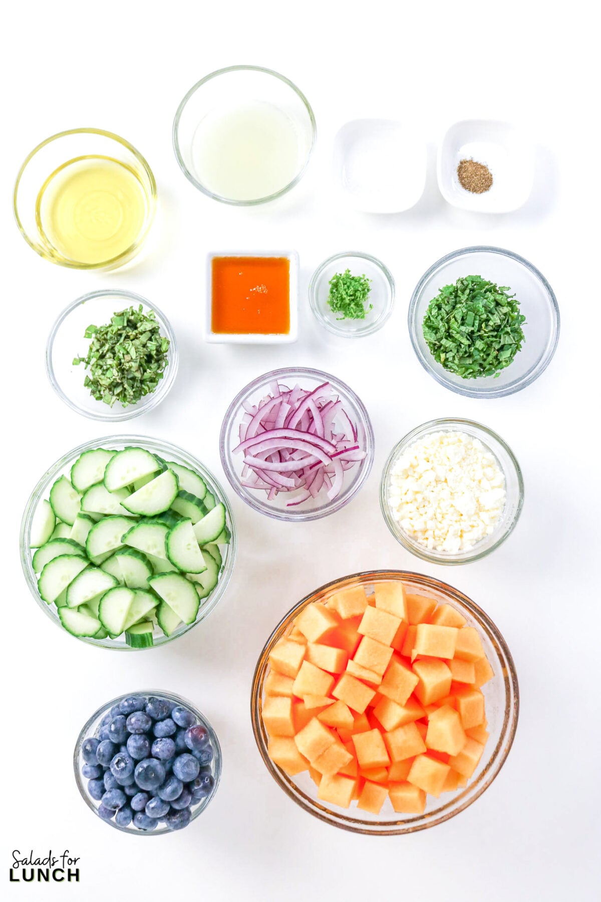Cantaloupe Cucumber Feta Salad - Cantaloupe Salad Ingredients Bowls of cubed cantaloupe, sliced cucumber, blueberries, feta, red onion, mint, basil, olive oil, lime juice, honey, lime zest, salt, and pepper.