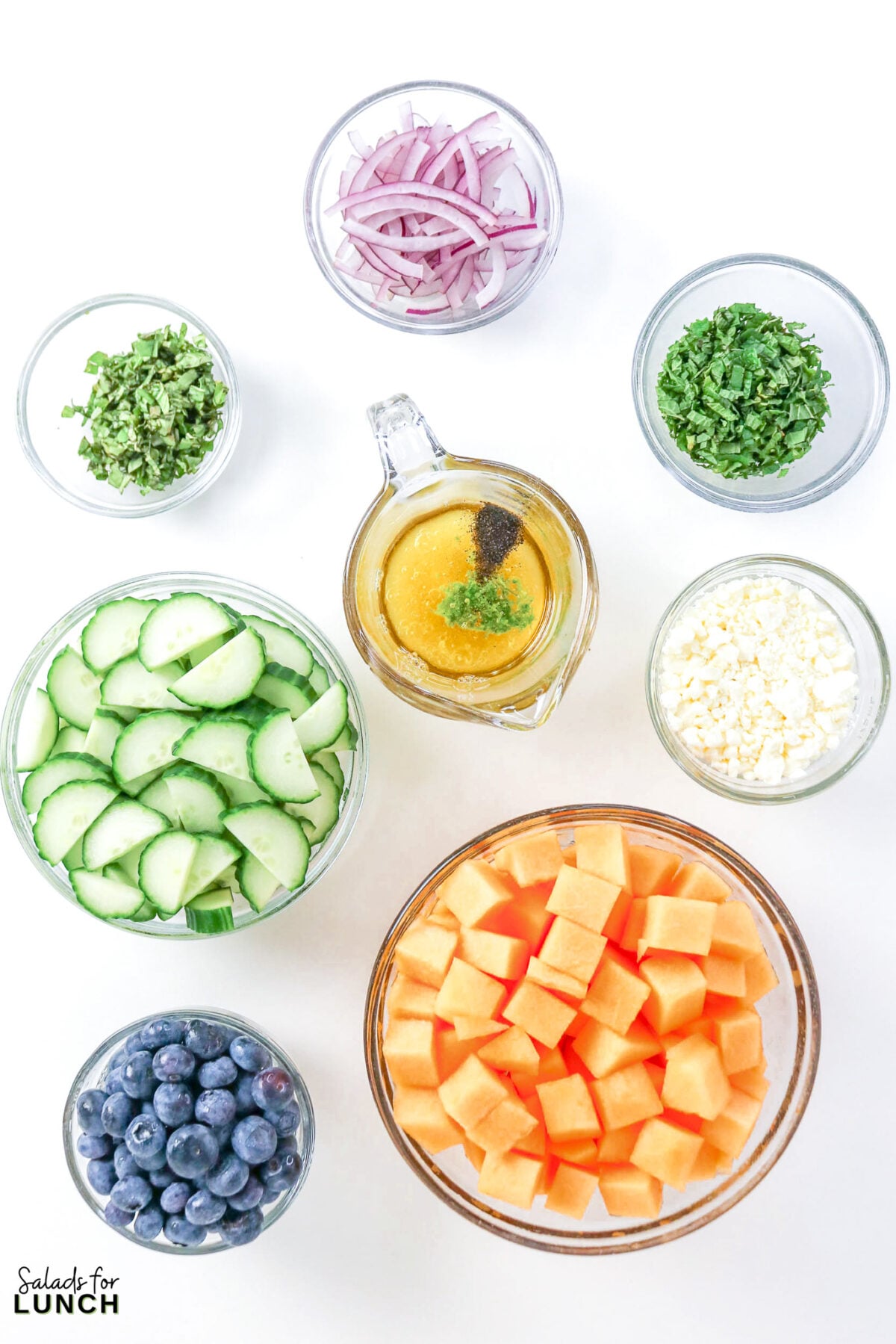 Cantaloupe Cucumber Feta Salad - Cantaloupe Salad Process 7 Bowls of cubed cantaloupe, sliced cucumber, blueberries, feta, red onion, mint, basil, and honey lime dressing arranged for the salad.